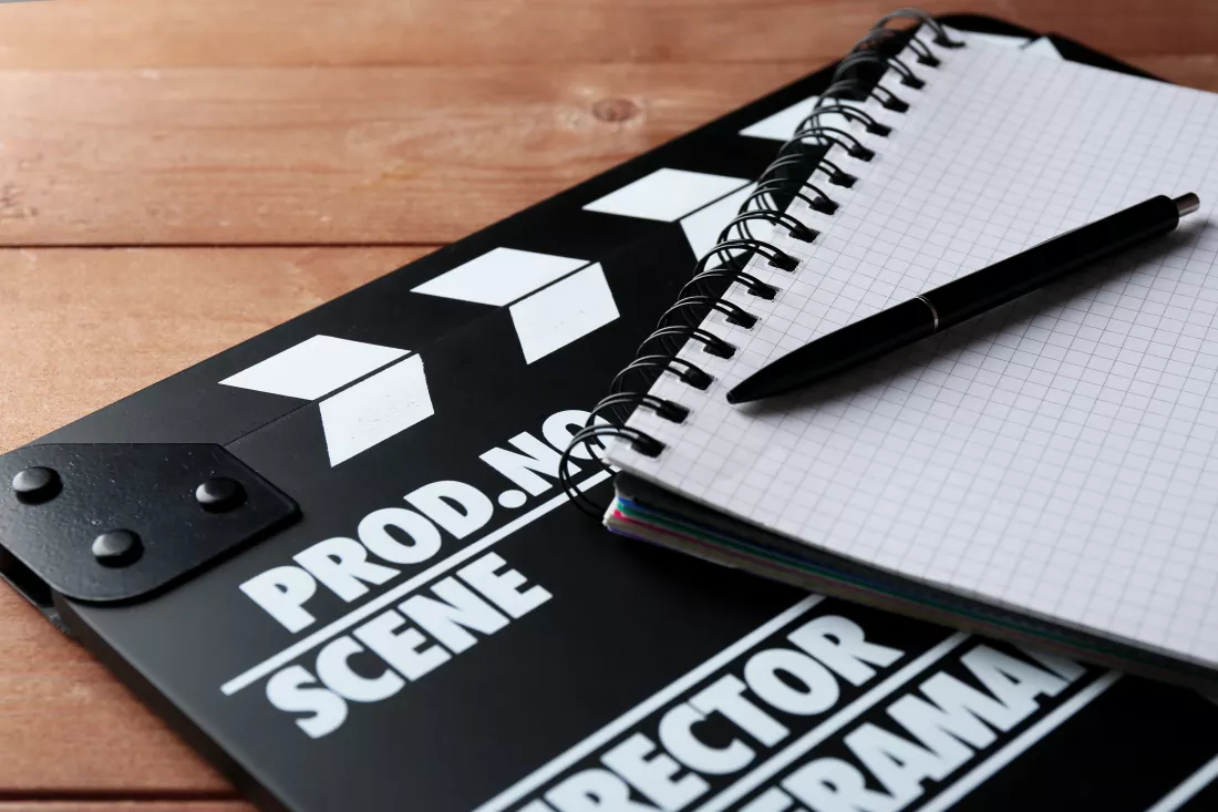 movie-clapper-with-notebook-pen-wooden-background