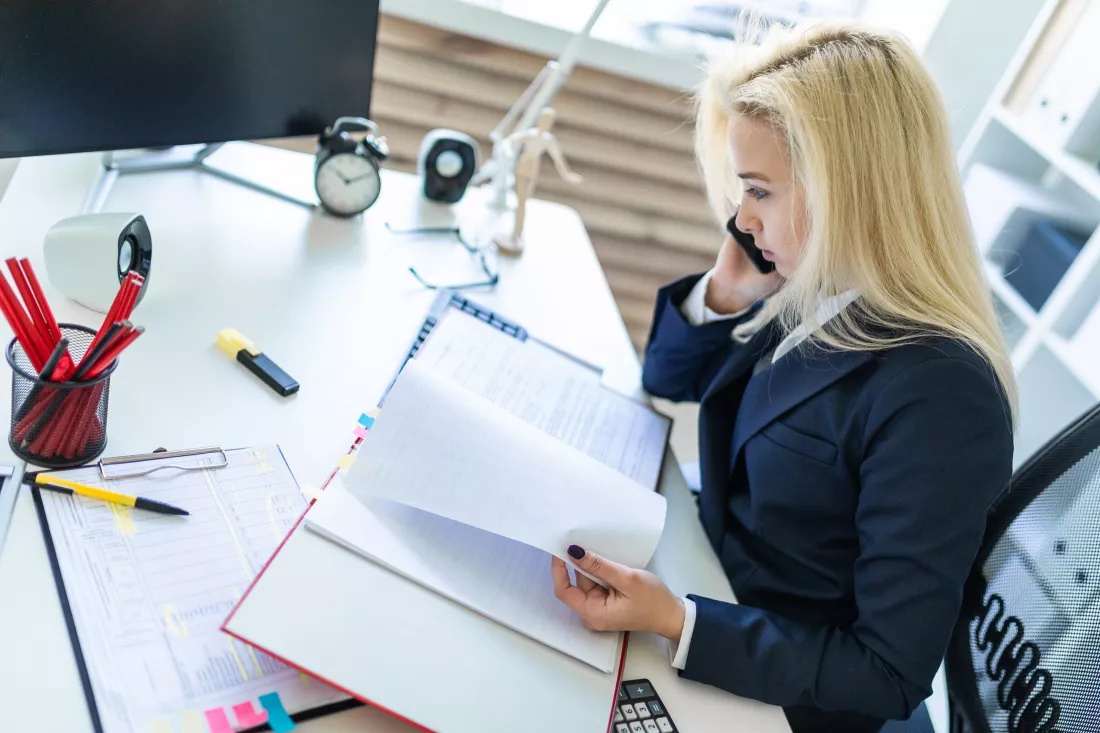 young-girl-sitting-desk-office-talking-phone-looking-documents